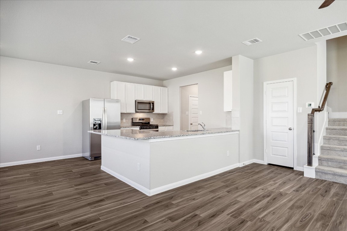 715 Gavin Walker Drive Rosharon, TX 77583 - Photo 4 of 15 This modern kitchen features an open layout with sleek granite countertops, stainless steel appliances, and ample cabinet space. The adjacent living area has wood-style flooring and neutral walls, offering a versatile and inviting space.