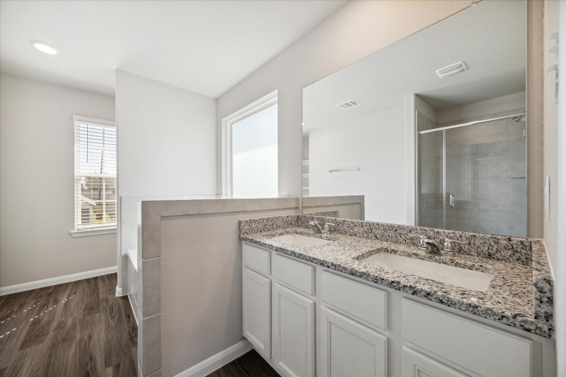 715 Gavin Walker Drive Rosharon, TX 77583 - Photo 7 of 15 This bathroom features a modern design with a double sink vanity topped with granite, a spacious glass-enclosed shower, and large windows providing natural light. The neutral color scheme and wood-style flooring add a touch of elegance.