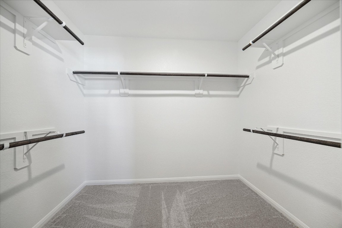 715 Gavin Walker Drive Rosharon, TX 77583 - Photo 8 of 15 This is a spacious walk-in closet with multiple hanging rods, neutral carpeting, and white walls, offering ample storage and a clean, bright appearance.