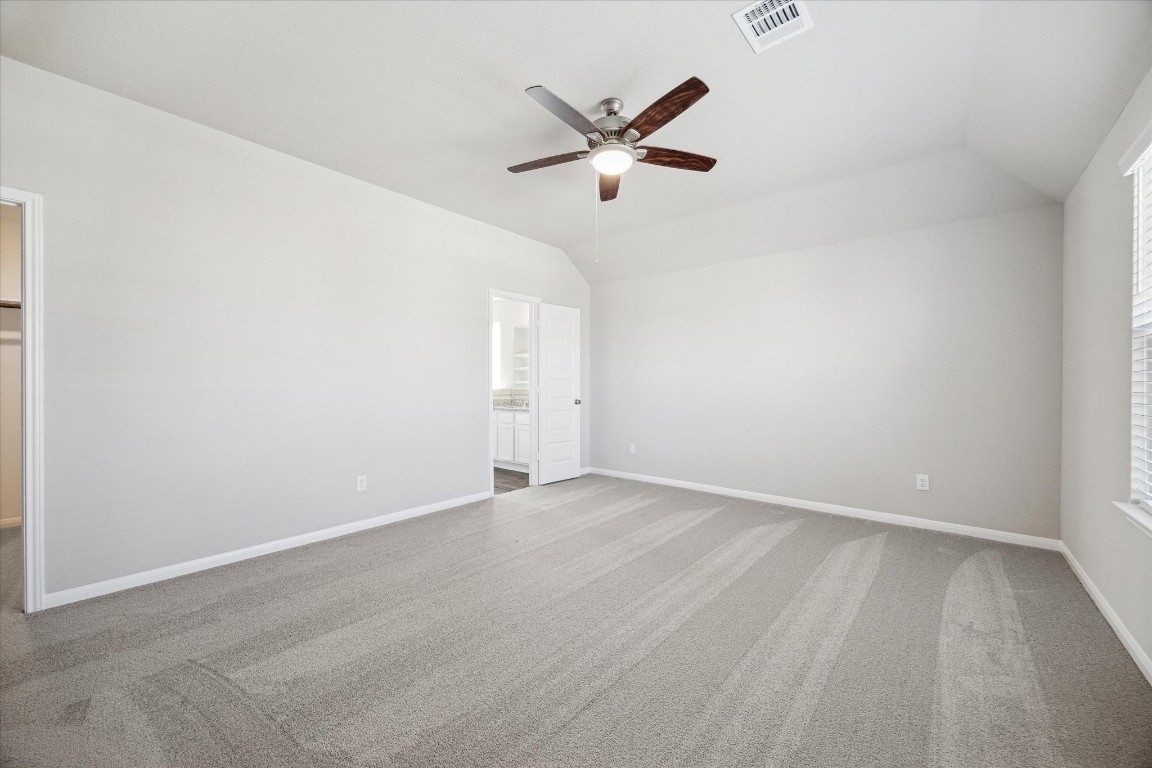 715 Gavin Walker Drive Rosharon, TX 77583 - Photo 9 of 15 This spacious bedroom features neutral walls, a ceiling fan, large windows for natural light, and an en-suite bathroom with a visible vanity. Perfect for comfort and convenience.