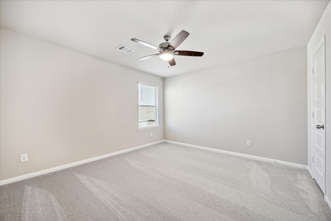 715 Gavin Walker Drive Rosharon, TX 77583 - Photo 10 of 15 This photo shows a spacious, carpeted room with neutral-colored walls. It features a ceiling fan with light and a window allowing natural light. A closed door is visible, suggesting closet or additional access. Perfect for a bedroom or office space.