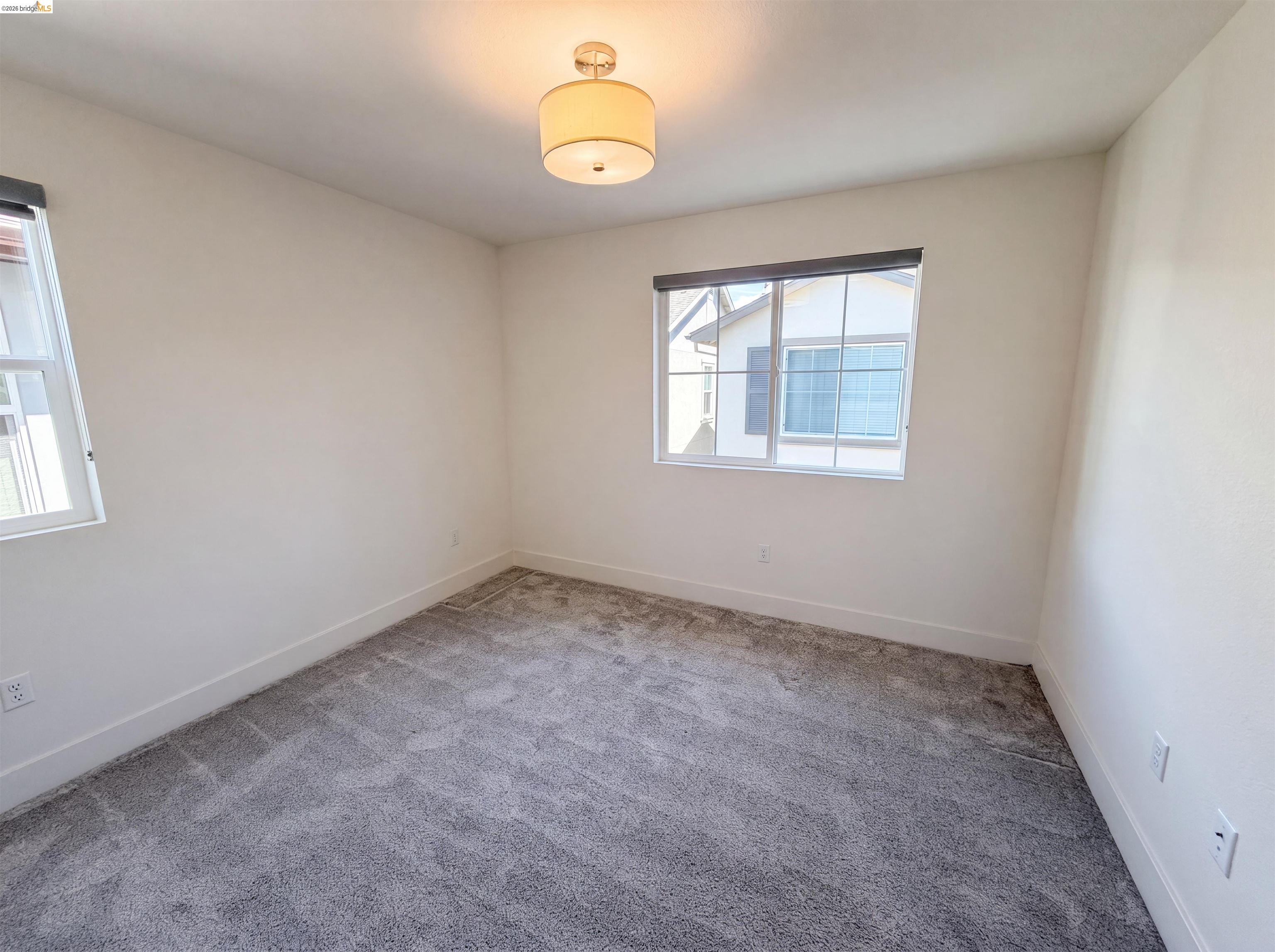 9034 Rudder Way Newark, CA 94560 - Photo 18 of 38 Interior room featuring light gray carpeting, white walls, two windows with dark roller shades, and a flush mount ceiling light fixture