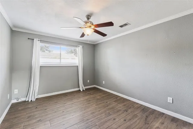 an empty room with wooden floor chandelier fan and windows