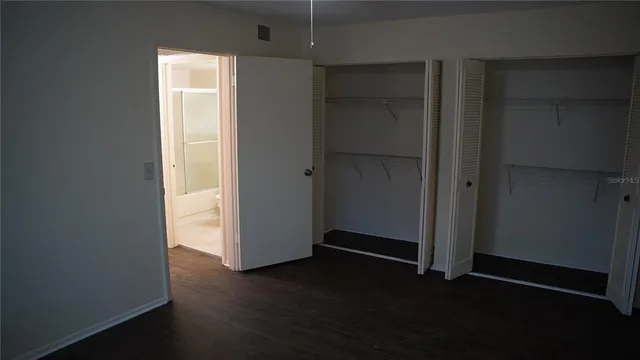 an empty room with wooden floor closet and windows