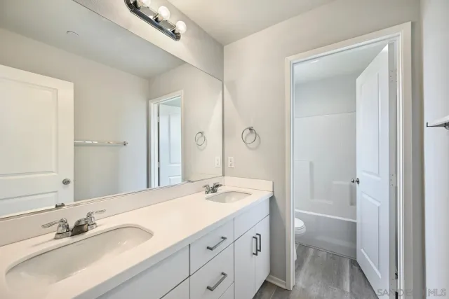 a bathroom with a double vanity sink and mirror with toilet