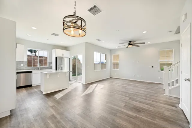 a view of an empty room and kitchen with wooden floor