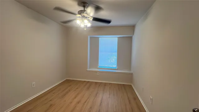 an empty room with wooden floor chandelier fan and window