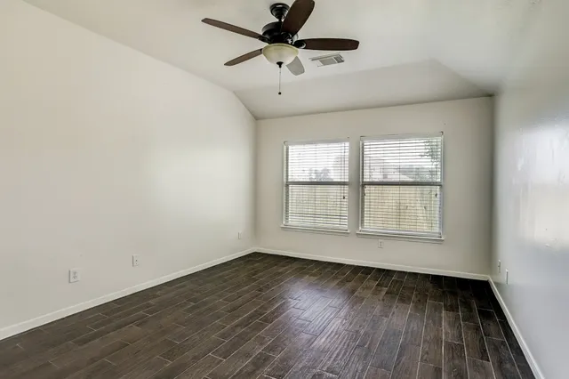 an empty room with wooden floor ceiling fan and windows