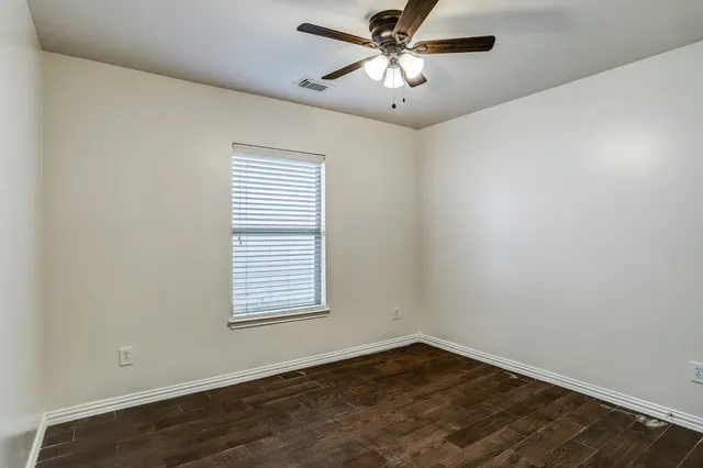 an empty room with wooden floor ceiling fan and windows
