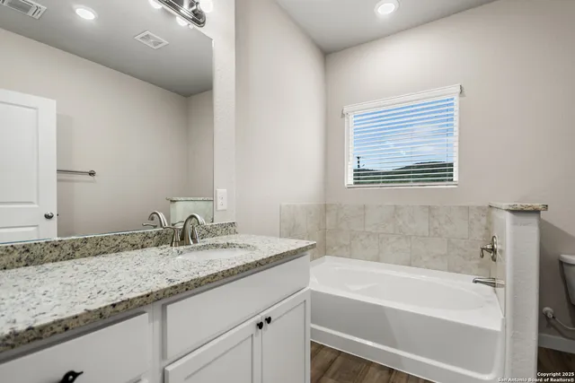 a bathroom with a granite countertop sink and a bathtub