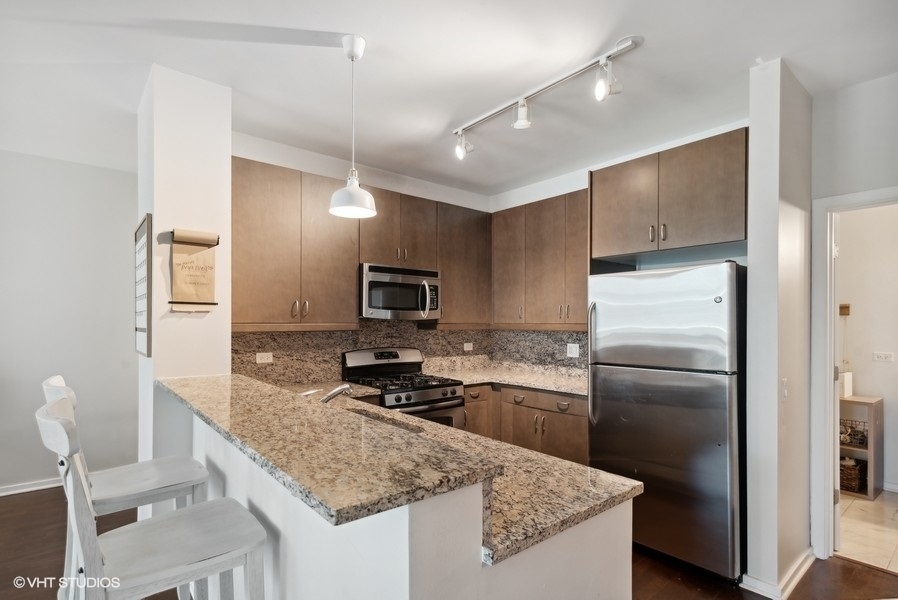 123 South Green Street, Unit 805B Chicago, IL 60607 - Photo 5 of 18 a kitchen with kitchen island granite countertop a refrigerator stove and sink