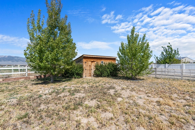 444 South Saddle Road Grantsville, UT 84029 - Photo 24 of 33 Wood-sided storage shed with a shingle roof and a single window, framed by mature trees and shrubs