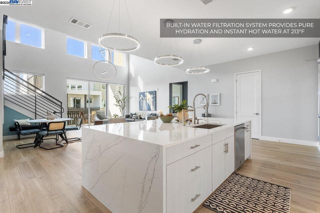 a kitchen with stainless steel appliances granite countertop a stove a sink a microwave a refrigerator and white cabinets with wooden floor