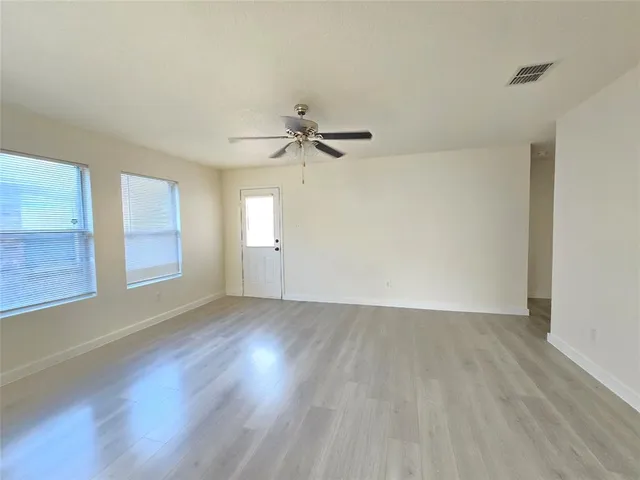 an empty room with wooden floor fan and windows