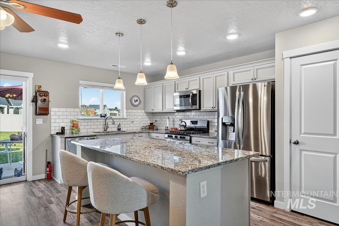 3174 North Greengate Way Star, ID 83669 - Photo 7 of 35 Kitchen with appliances with stainless steel finishes, a kitchen breakfast bar, light stone countertops, decorative light fixtures, and a center island