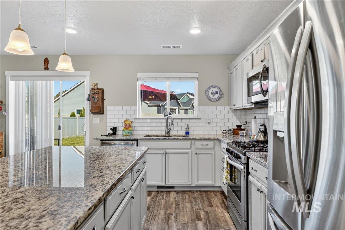 3174 North Greengate Way Star, ID 83669 - Photo 8 of 35 Kitchen featuring appliances with stainless steel finishes, light stone countertops, tasteful backsplash, hanging light fixtures, and a textured ceiling