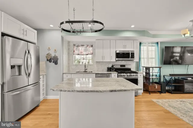 a kitchen with stainless steel appliances granite countertop a refrigerator a stove a sink a microwave a dining table and chairs with wooden floor