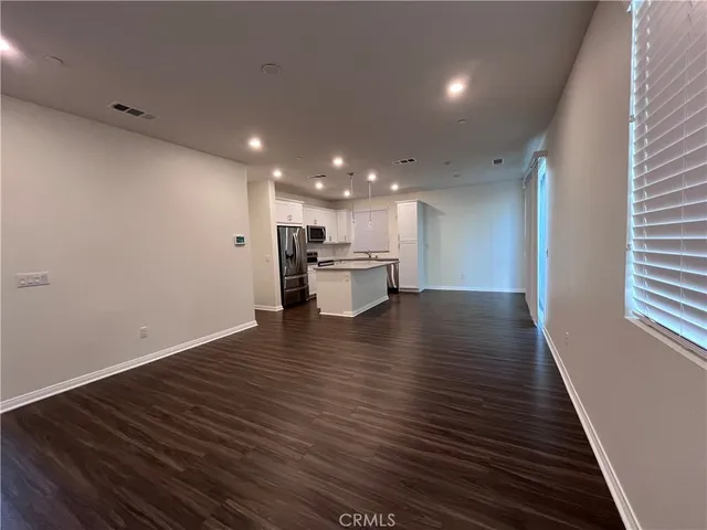 an empty room with wooden floor kitchen view and a window