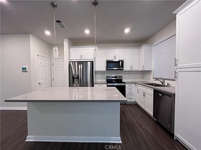 a large kitchen with kitchen island a stove a sink a refrigerator and white cabinets with wooden floor