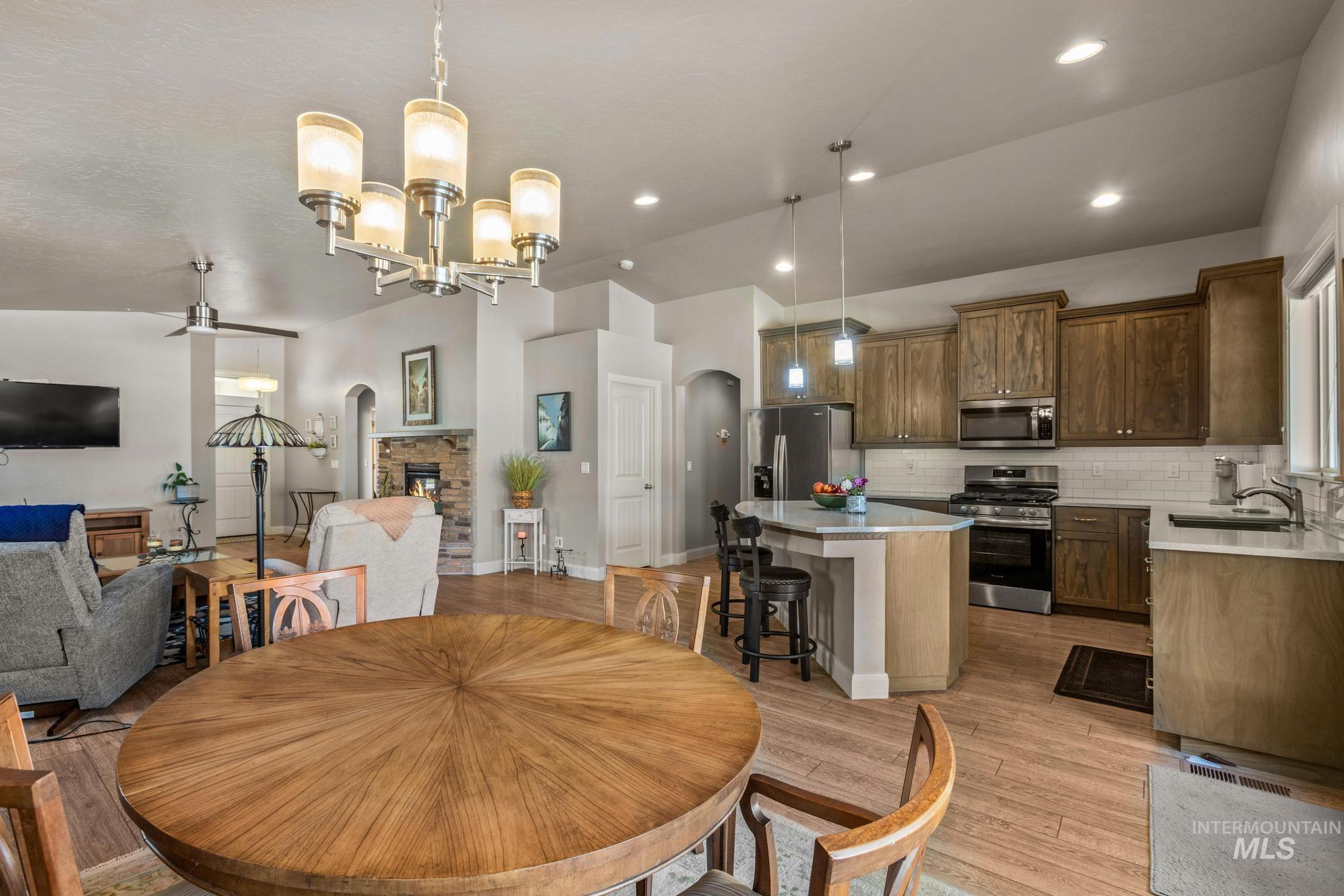 5832 West Rotherham Drive Eagle, ID 83616 - Photo 12 of 42 Dining area with arched walkways, lofted ceiling, a chandelier, light wood-style floors, and a stone fireplace