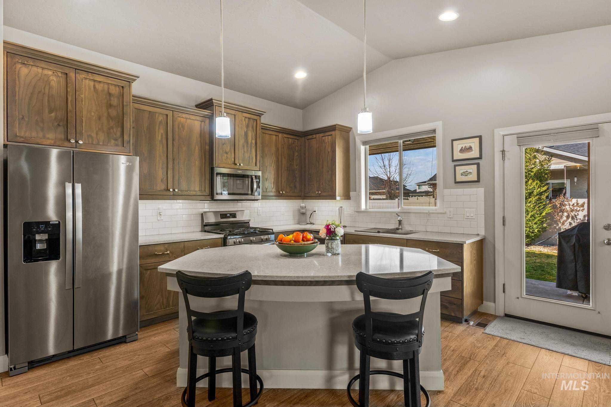 5832 West Rotherham Drive Eagle, ID 83616 - Photo 13 of 42 Kitchen featuring stainless steel appliances, lofted ceiling, backsplash, a kitchen bar, and light wood-type flooring