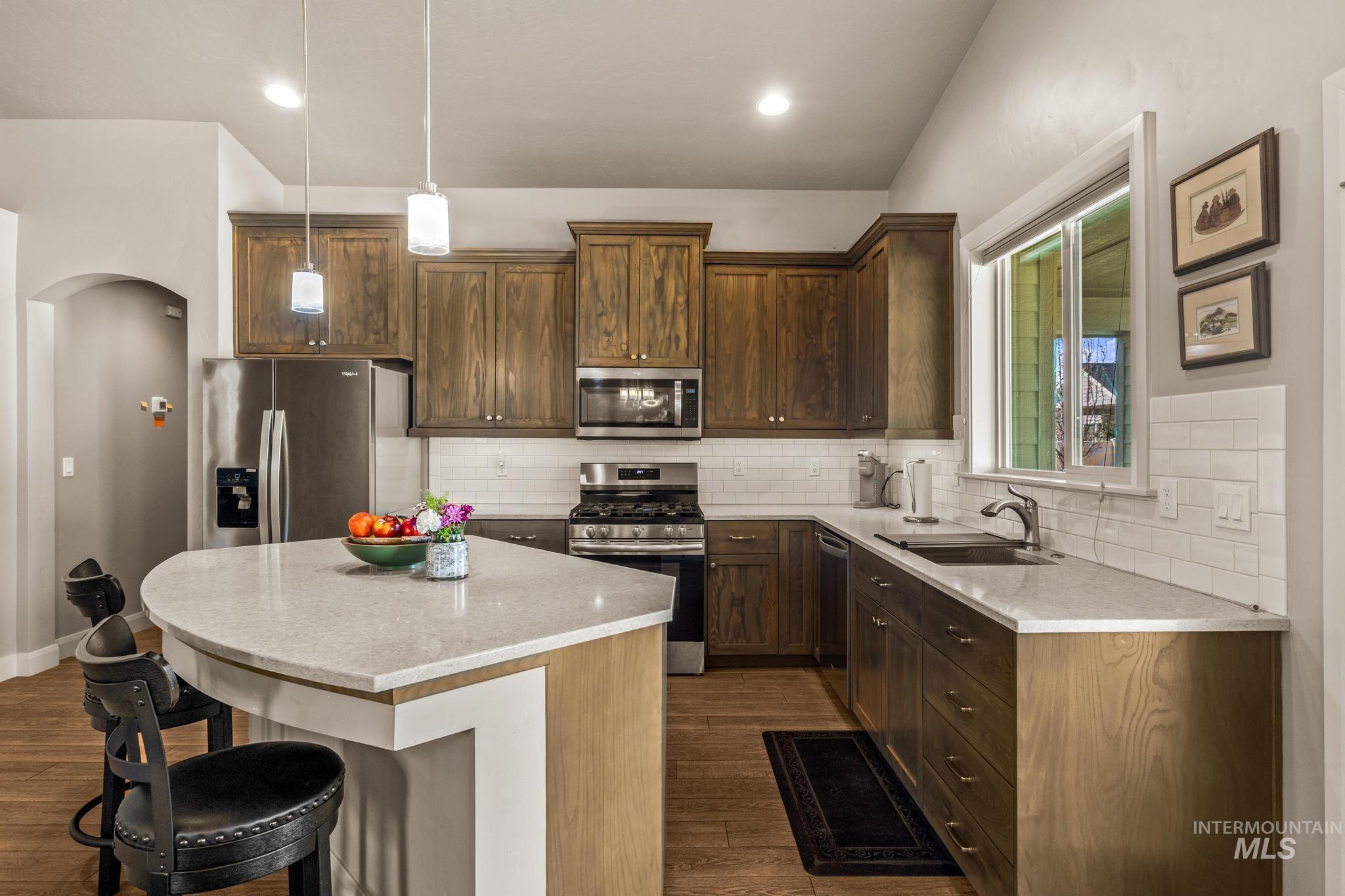 5832 West Rotherham Drive Eagle, ID 83616 - Photo 14 of 42 Kitchen featuring stainless steel appliances, arched walkways, a center island, light stone counters, and a kitchen bar