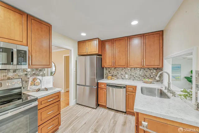 a kitchen with stainless steel appliances granite countertop a refrigerator a stove top oven a sink and dishwasher with wooden floor