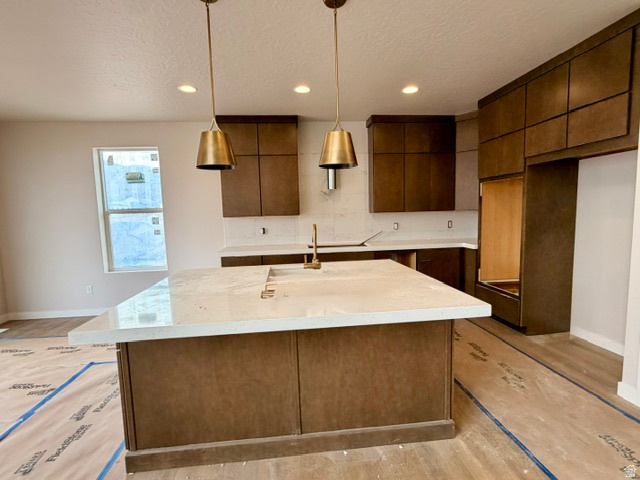 5885 Canyon Rim Road, Unit 624 Lehi, UT 84048 - Photo 2 of 10 Kitchen featuring a large island with a light-toned countertop, brass-toned pendant lighting, wood-finish cabinetry, white tile backsplash, and recessed lighting