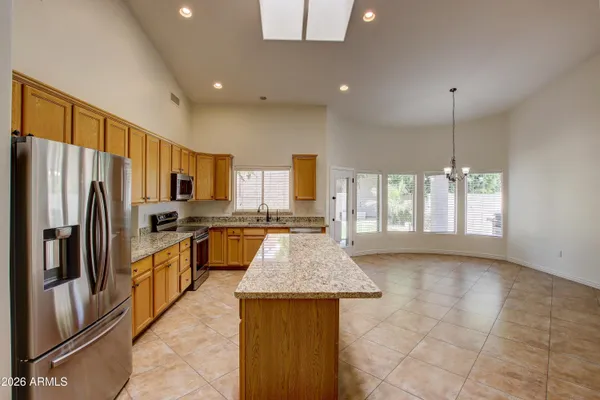 a kitchen with stainless steel appliances granite countertop a refrigerator a sink dishwasher a stove and a dining table with wooden floor