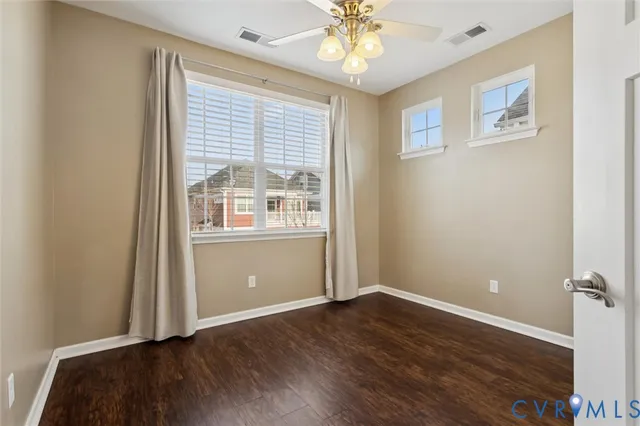 an empty room with wooden floor chandelier fan and windows