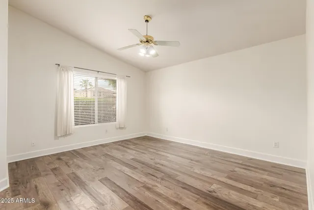 an empty room with wooden floor chandelier fan and windows