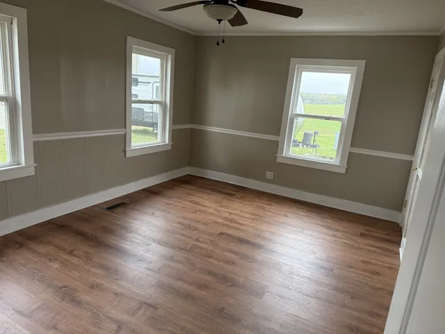 an empty room with wooden floor cabinet and windows
