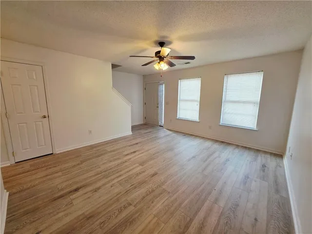 an empty room with wooden floor ceiling fan and windows