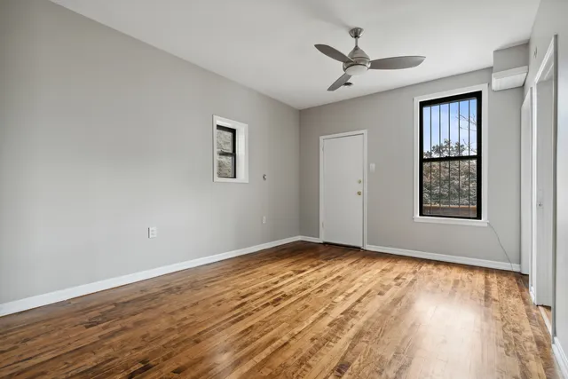 an empty room with wooden floor ceiling fan and windows