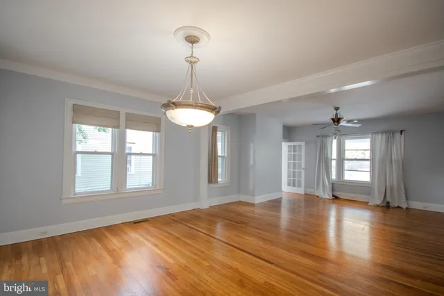 an empty room with wooden floor chandelier and windows