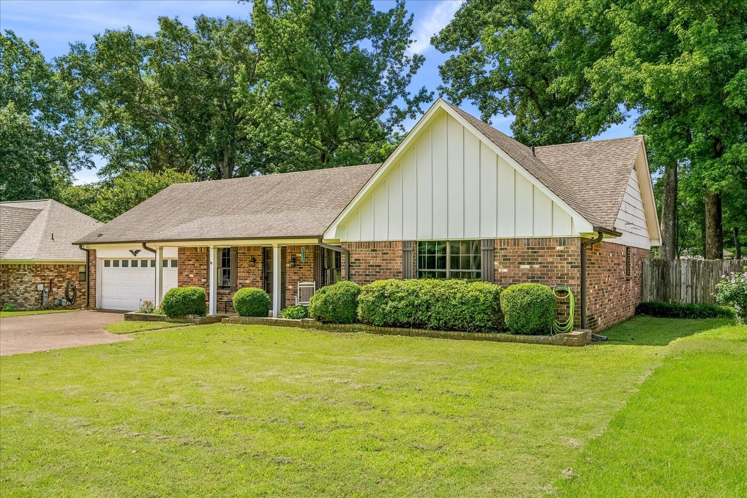 5711 Yale Road Bartlett, TN 38134 - Photo 26 of 29 Brick exterior with white vertical siding gables, featuring a covered front porch, an attached two-car garage, and a lush front lawn with established foundation plantings