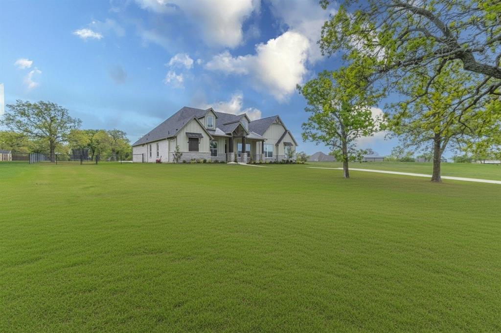 Expansive manicured lawn surrounding a contemporary residence featuring a stone and stucco exterior, dark shingle roof, covered front entry, and multiple windows