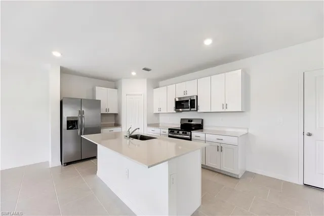 a kitchen with stainless steel appliances a stove top oven a sink a refrigerator white cabinets and wooden floor