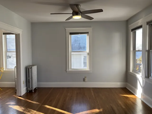 an empty room with wooden floor a ceiling fan and windows