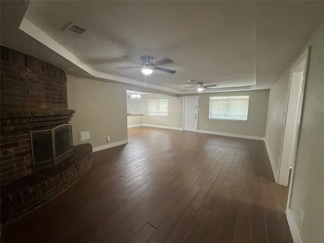 an empty room with wooden floor fireplace and windows