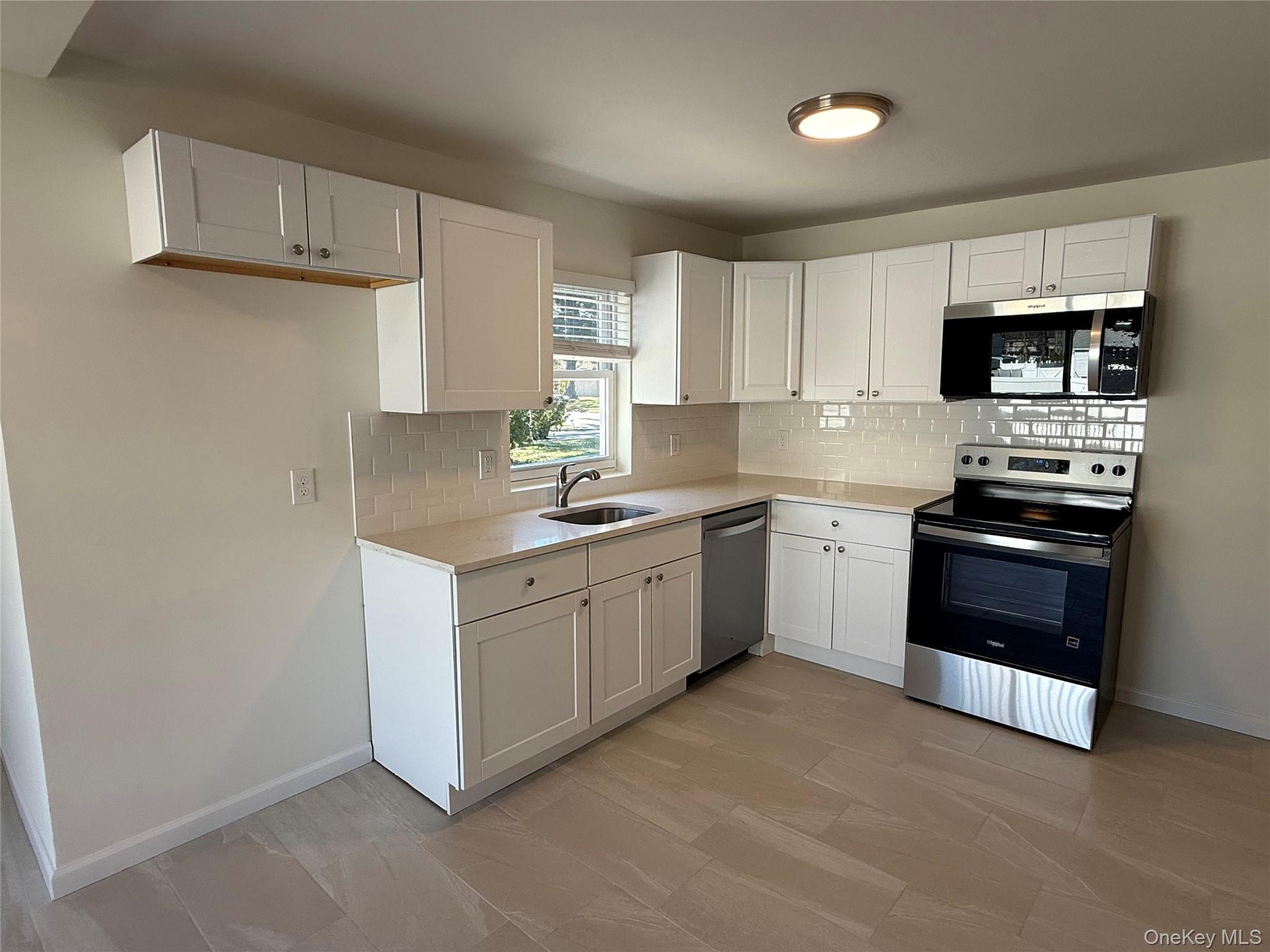 225 Fir Grove Road Ronkonkoma, NY 11779 - Photo 7 of 22 a kitchen with stainless steel appliances white cabinets a sink a stove a microwave and wooden floors
