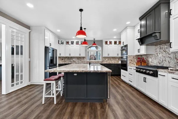 a kitchen with stainless steel appliances granite countertop a stove top oven a sink dishwasher and a refrigerator with wooden floor