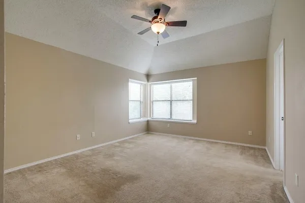 an empty room with chandelier fan and windows