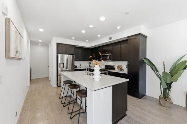 a kitchen with stainless steel appliances kitchen island granite countertop a sink a stove a refrigerator and a dining table with wooden floor