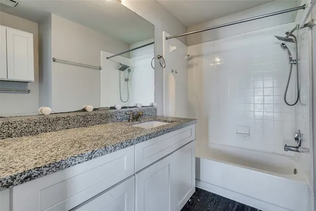 a bathroom with a granite countertop sink a mirror a bathtub and shower