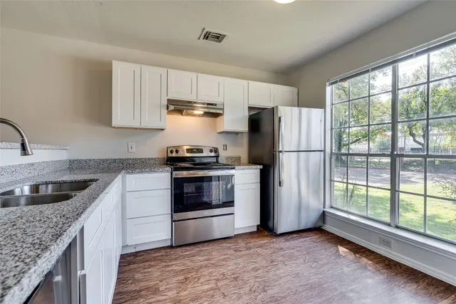 a kitchen with granite countertop a refrigerator a sink a stove and white cabinets