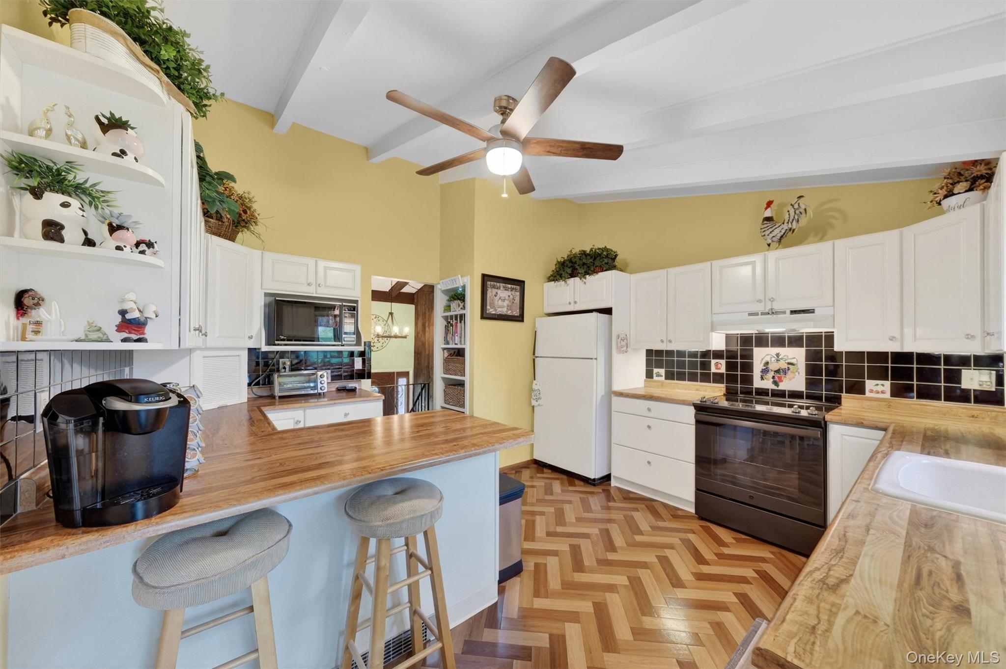 1 Rockledge Road Poughkeepsie, NY 12601 - Photo 9 of 36 Kitchen featuring vaulted ceilings with exposed beams, wood-finish flooring in a herringbone pattern, white cabinetry, breakfast bar, tile backsplash, cabinet lighting and light wood-finish countertops