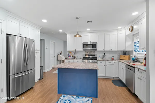 a kitchen with stainless steel appliances granite countertop a refrigerator a sink dishwasher a stove and white countertops with wooden floor