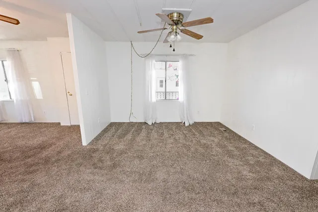 a view of an empty room with window and chandelier fan