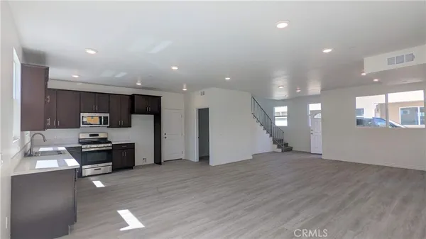a kitchen with stainless steel appliances kitchen island granite countertop a stove top oven a sink a refrigerator and white cabinets with wooden floor